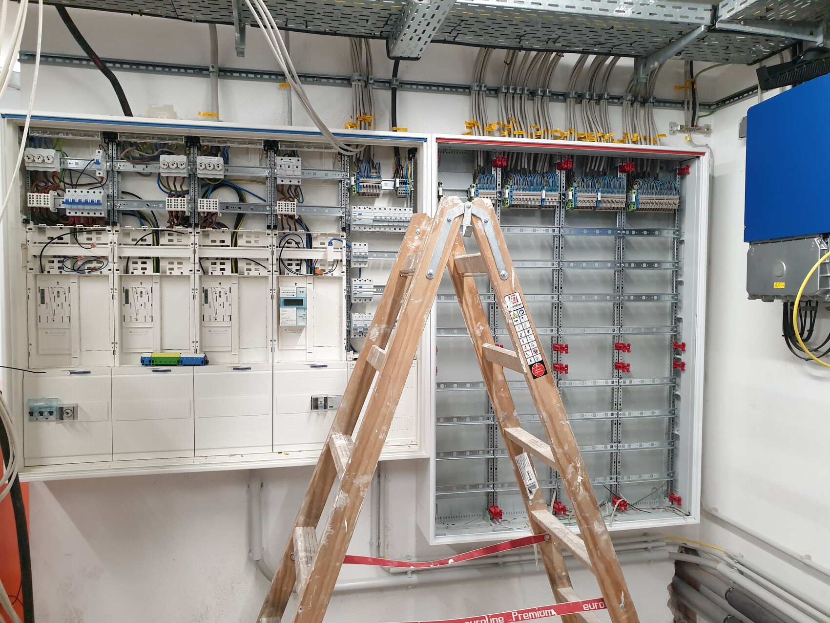 Offenes Schalttafelsystem mit Kabelbündeln; Holzleiter im Vordergrund.
