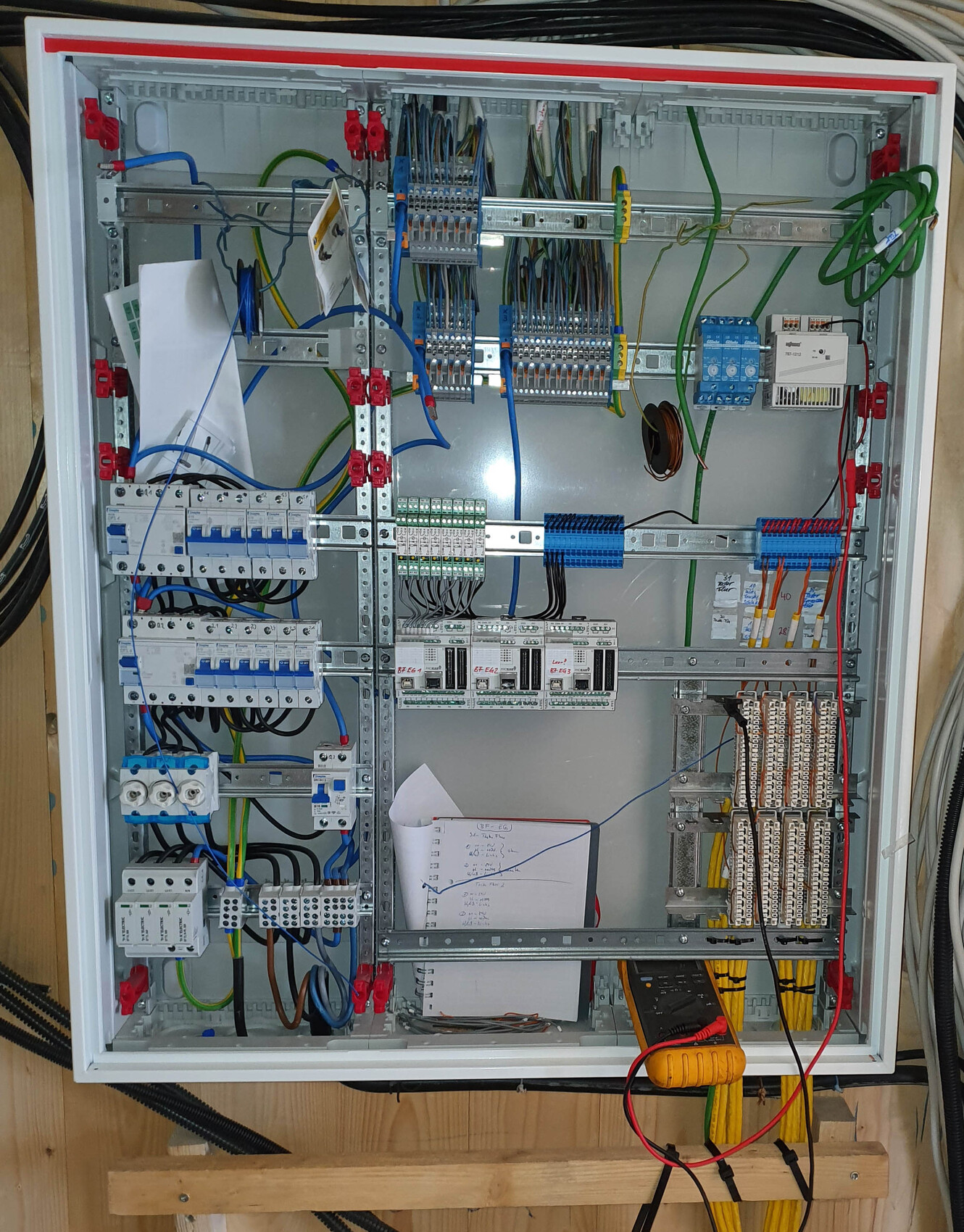 Offener elektrischer Schaltschrank mit Verdrahtung, Klemmen und Messgerät.