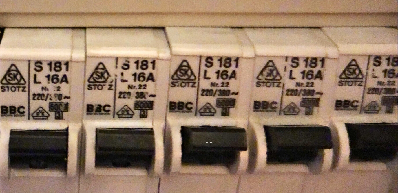 Reihe weißer Sicherungsautomaten in einem Verteilerkasten mit schwarzen Hebeln.