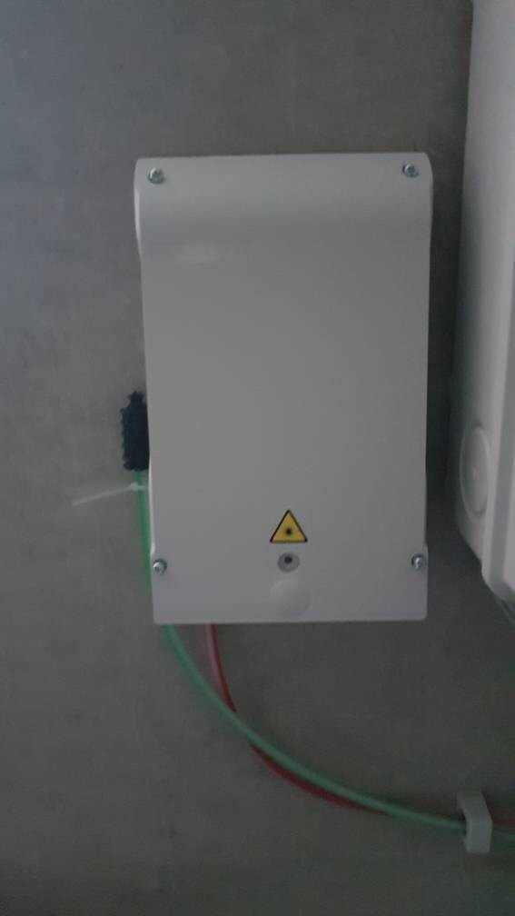 Wandmontierter elektrischer Verteilerkasten mit Warnhinweis und grün-roten Kabeln.