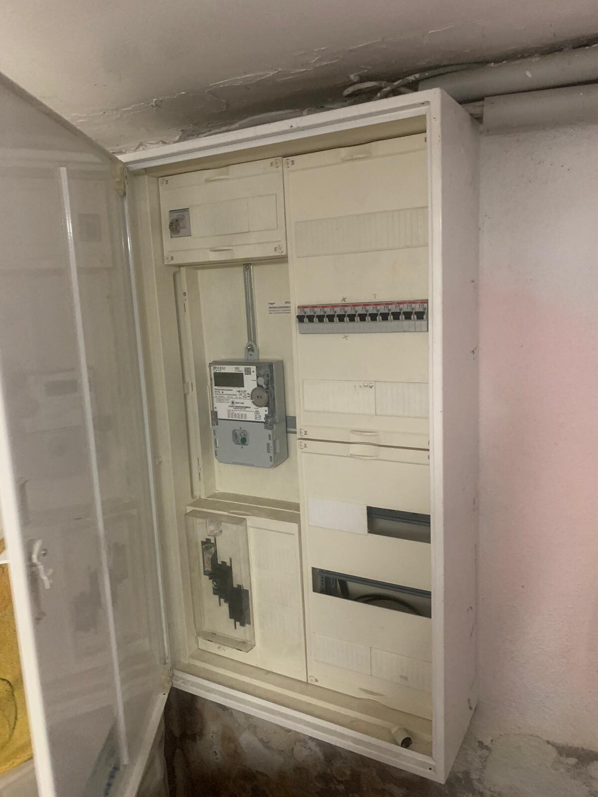 Offener Elektroverteilerkasten mit Zähler und mehreren Sicherungen, Tür geöffnet.