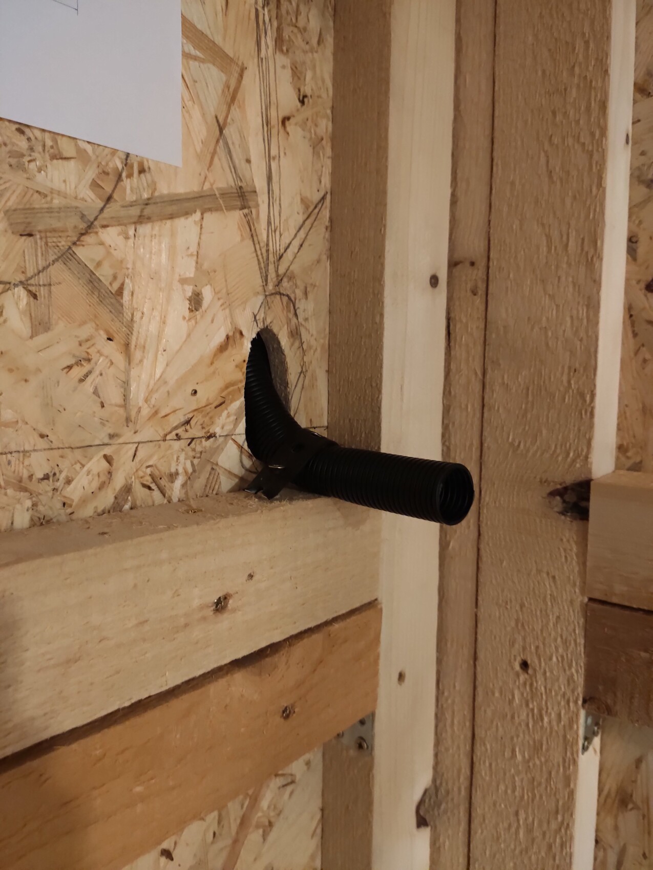 Schwarzes flexibles Rohr führt durch Loch in einer OSB-Wand einer Holzbaukonstruktion.