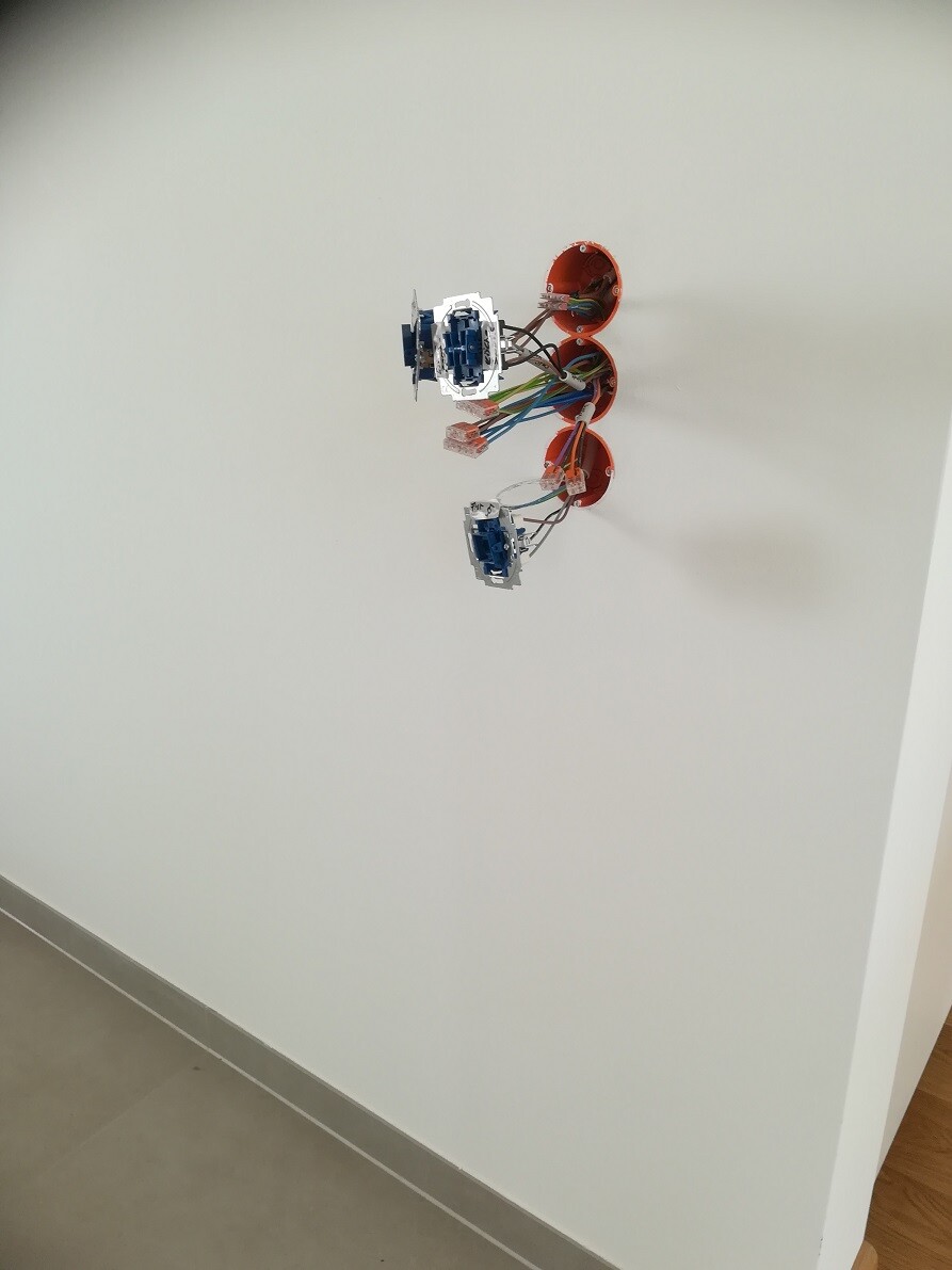 Offene Elektroverkabelung an der Wand: drei orange Dosen mit bunten Leitungen und blauen Bauteilen.