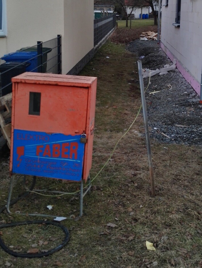 Oranger Elektro-Verteilerkasten auf Baustelle neben Hauswand mit Kabeln