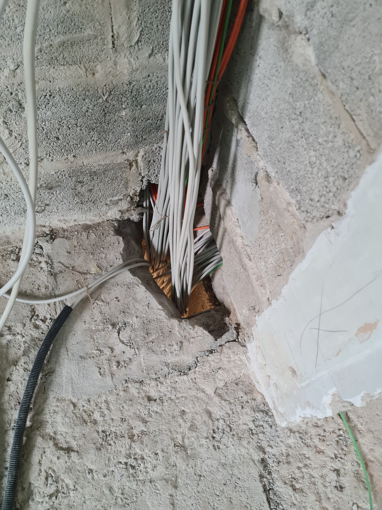 Kabelbündel in Lochöffnung einer rauen Betonwand auf einer Baustelle.