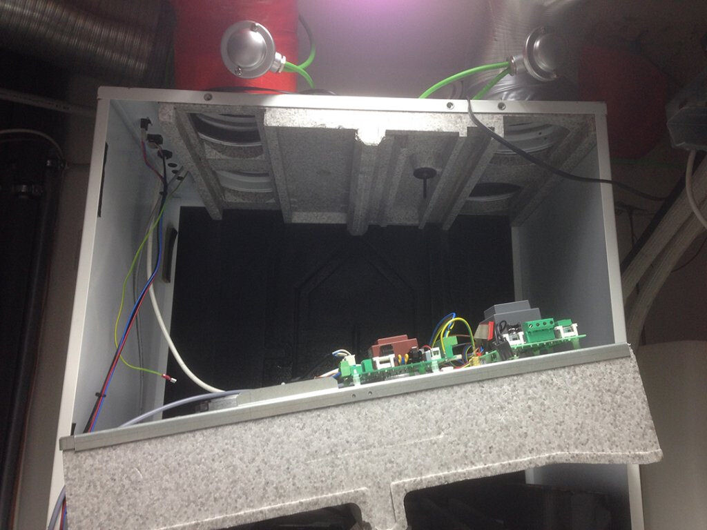 Offener Elektronikschrank mit Leiterplatten, Kabeln und grünen Anschlussklemmen.
