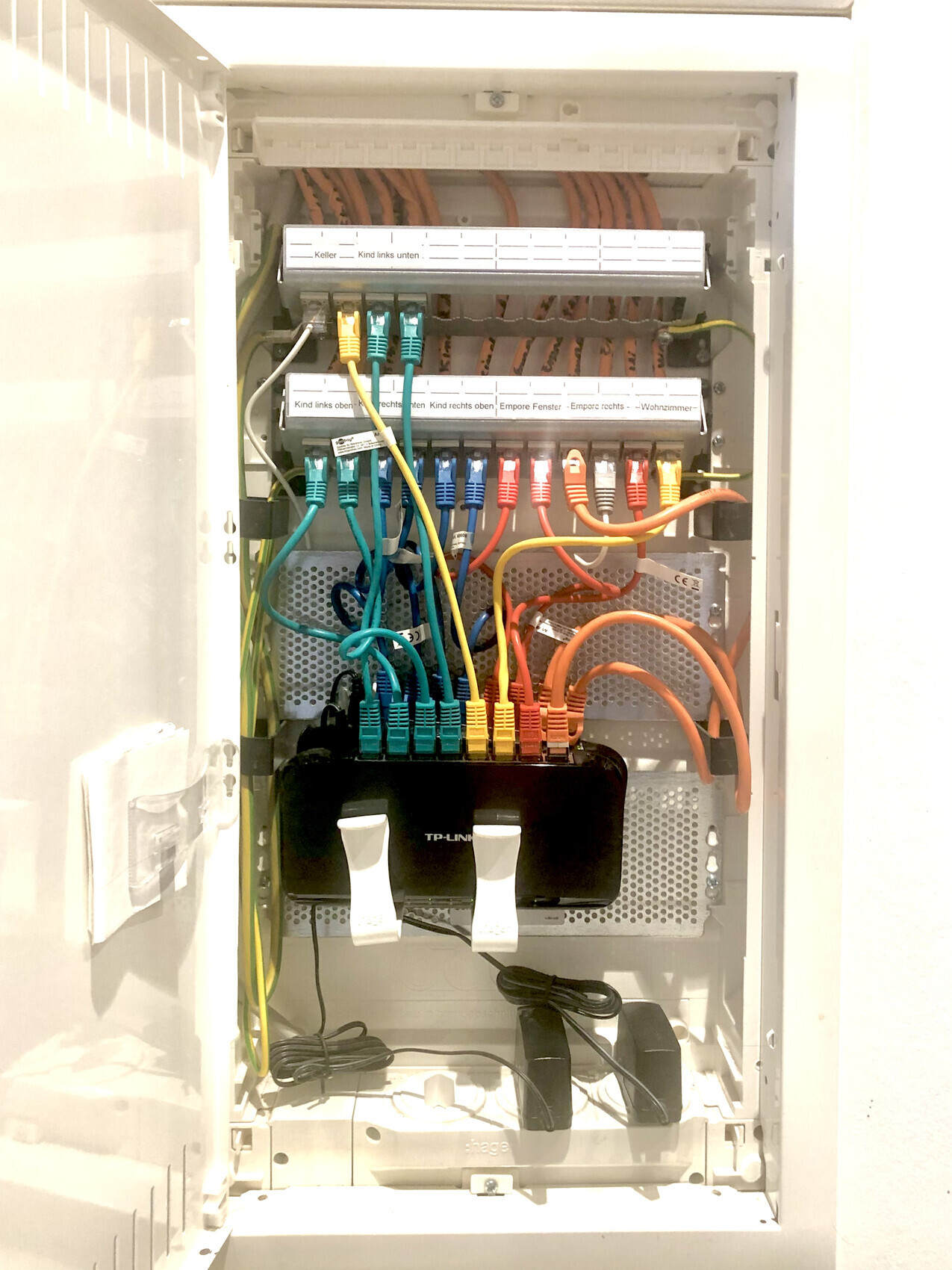 Offener Netzwerkschrank mit bunten RJ45-Kabeln, Patchpanels und TP-Link Switch.