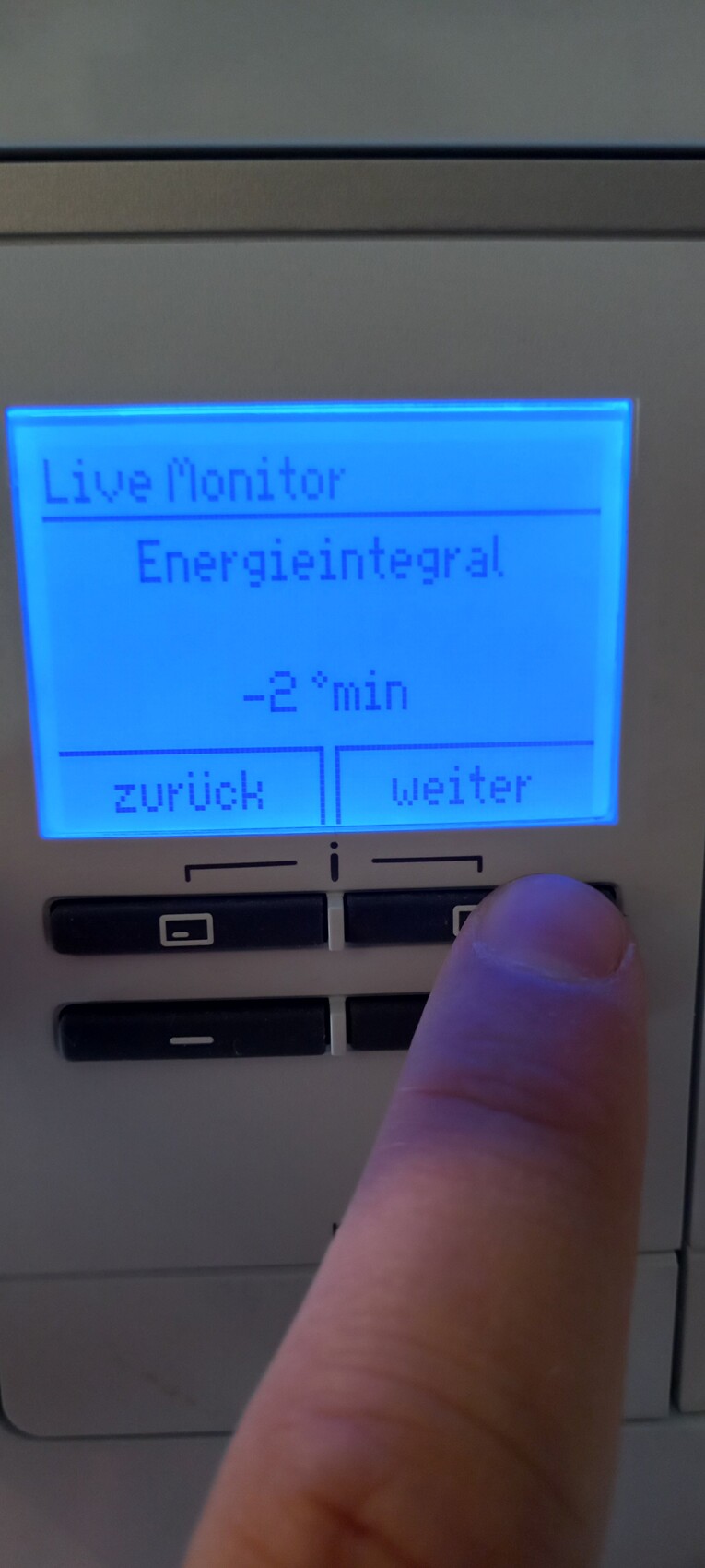 Blaues Display zeigt Live Monitor, Energieintegral; -2 min, Finger drückt Taste.