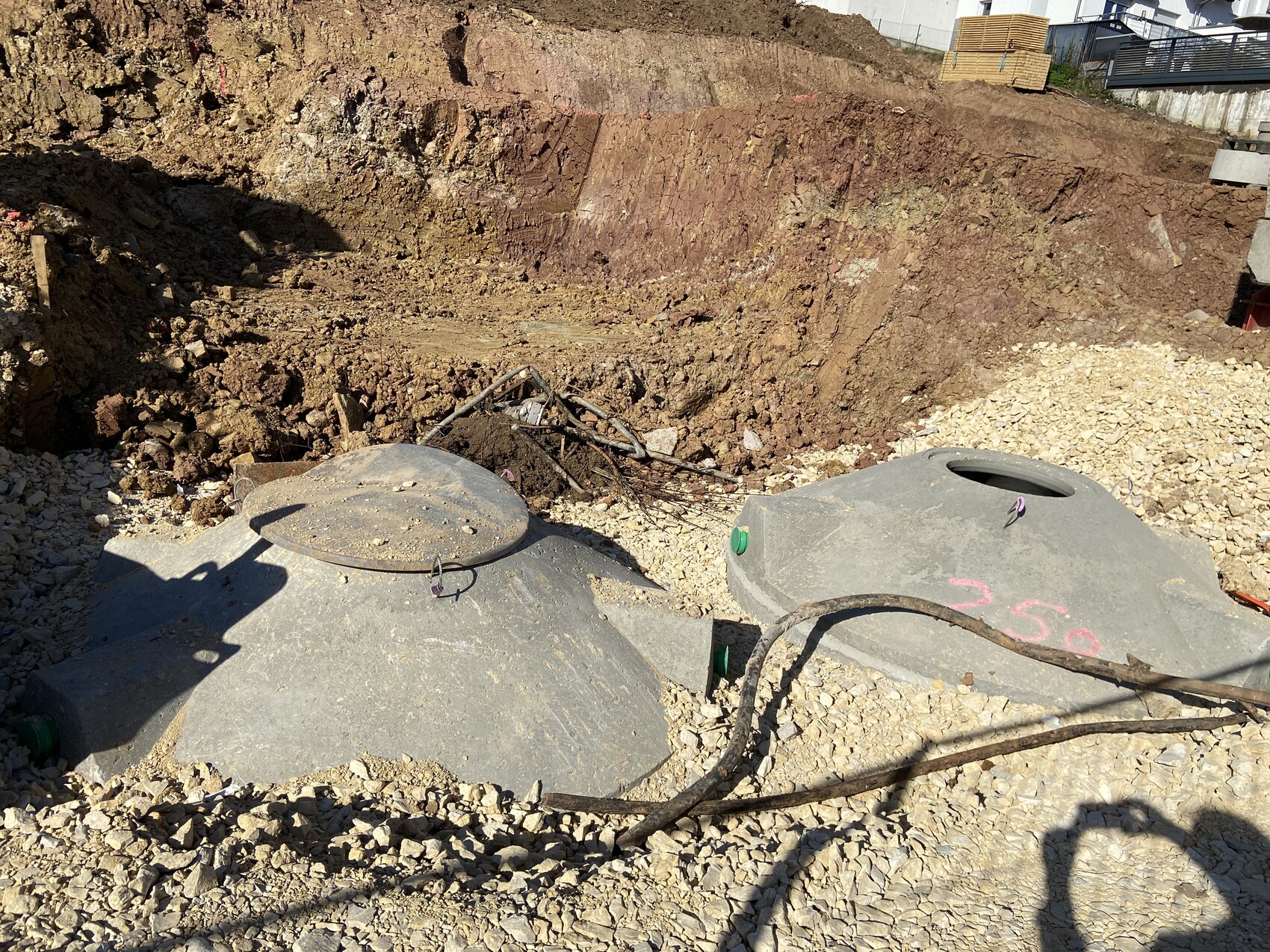 Baustelle: ausgehobene Grube mit zwei runden Beton-Schächten, Kies und Kabelreste.