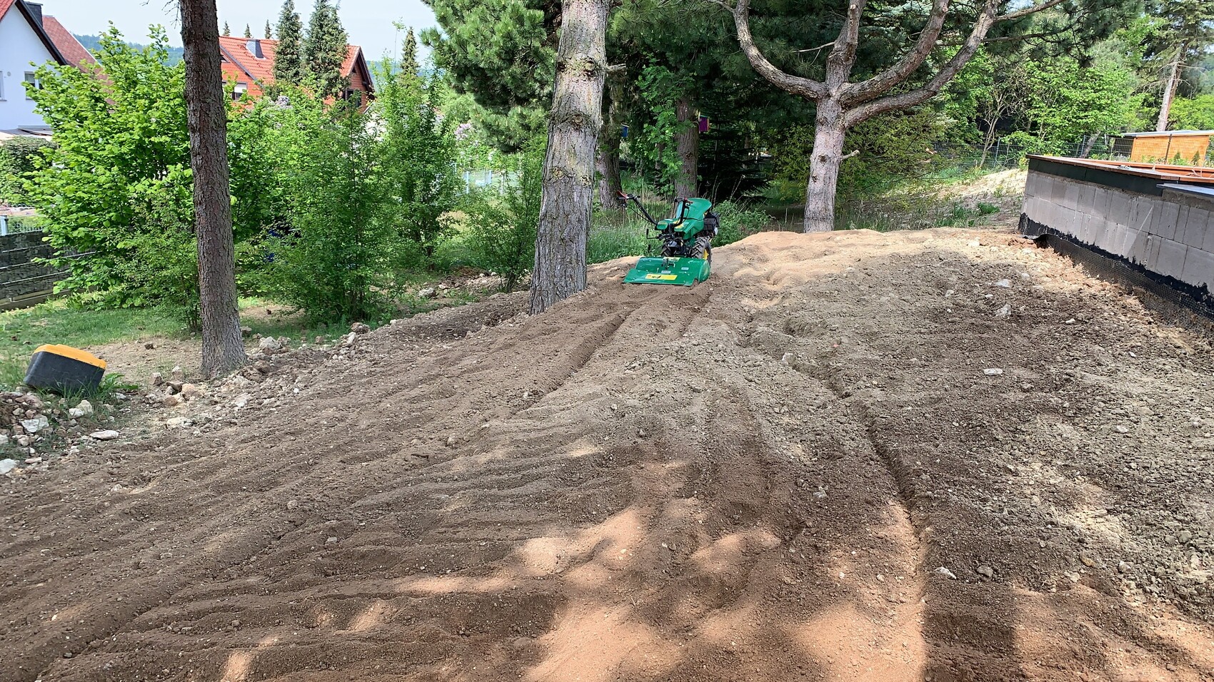 Großer Erdhaufen im Gartenbereich mit Baumaschine und Bäumen