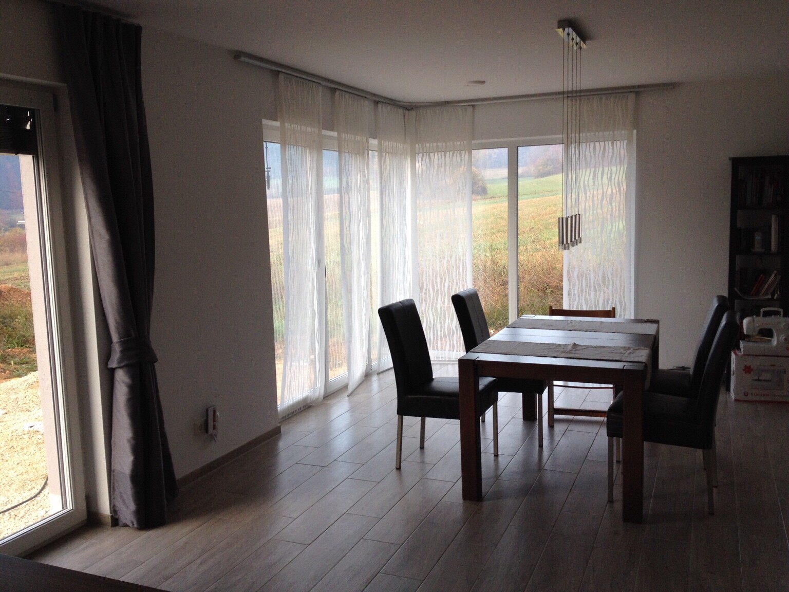 Esszimmer mit Holztisch, schwarzen Stühlen, großen Glasfenstern und weißen Vorhängen