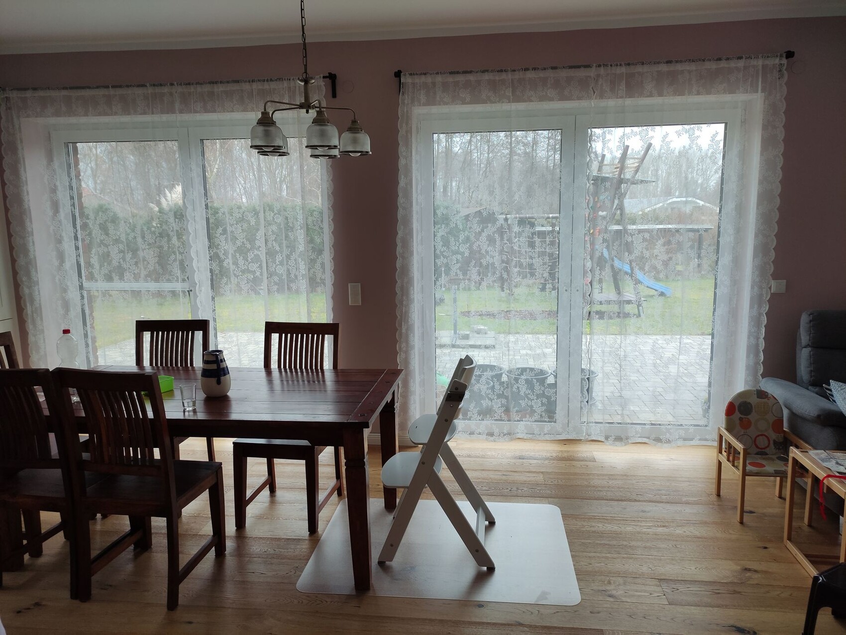 Esszimmer mit Holztisch, Stühlen und Kronleuchter; Glas-Tür mit Spitze; Garten mit Spielgerät.