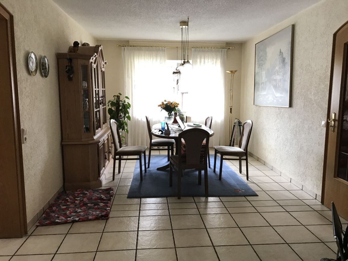 Esszimmer mit rundem Tisch, Stühlen, Blumenstrauss, Vorhängen und Sideboard
