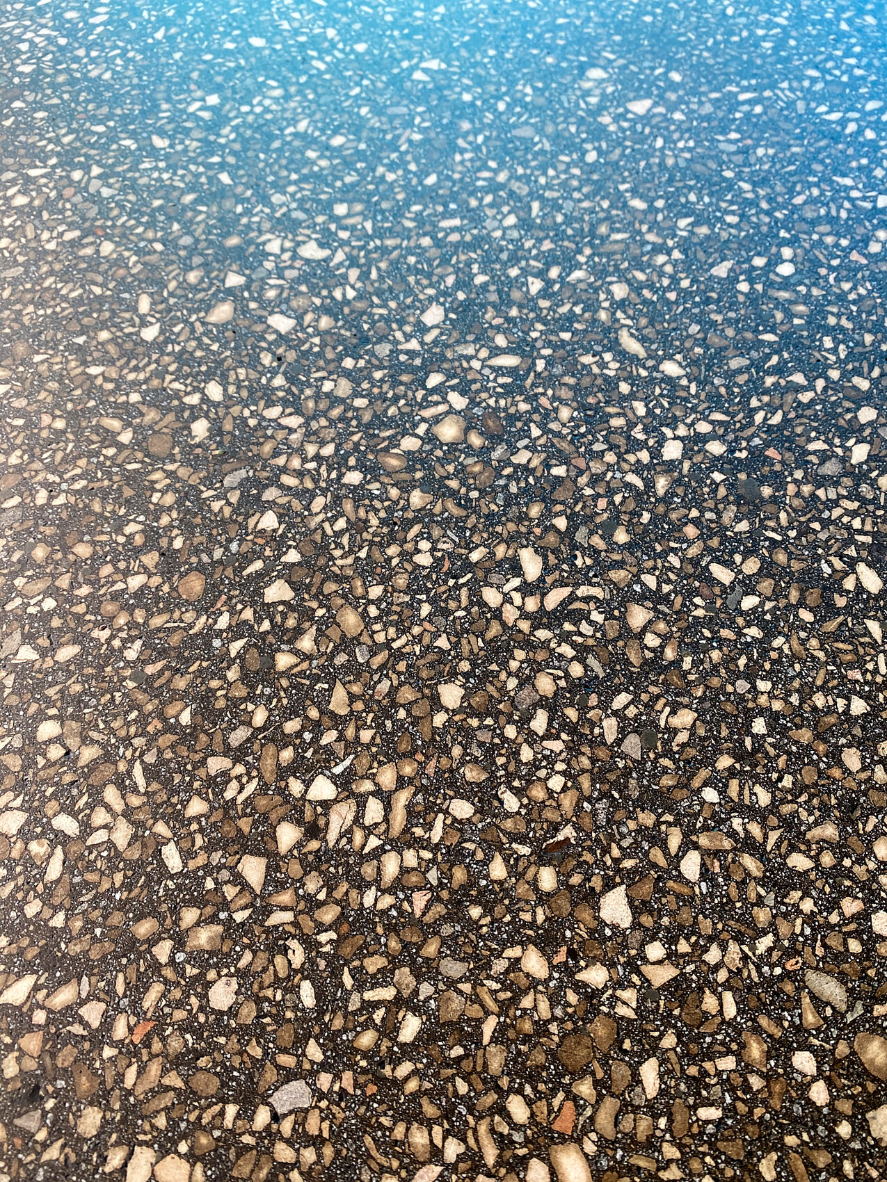 Nahaufnahme einer Kieseloberfläche mit vielen Steinchen; Farbübergang von Blau oben zu Braun unten.