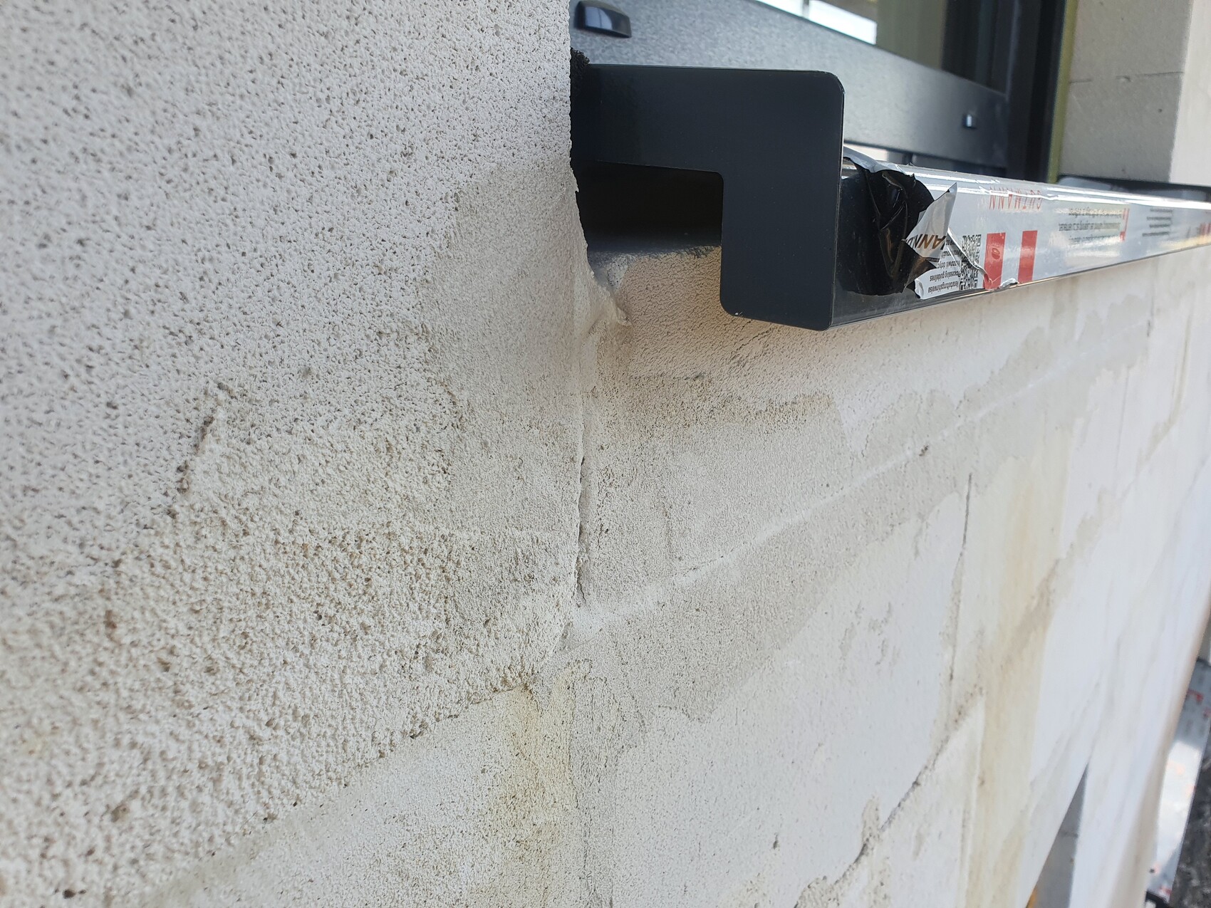 Beigefarbene Putzwand mit Rissen und Abplatzungen; schwarzer Fensterrahmen mit Klebeband.
