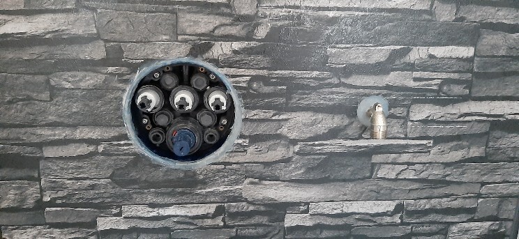 Rundes offenes Wandgehäuse in Steinwand mit mehreren Anschlüssen; daneben Wasserhahn.