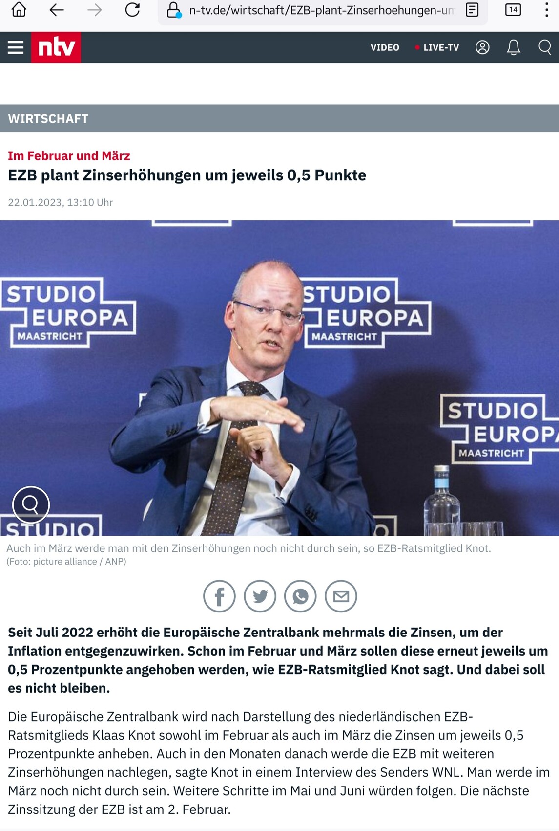 Mann im Anzug sitzt und gestikuliert, vor blauem Hintergrund mit Studio Europa Maastricht Logos.