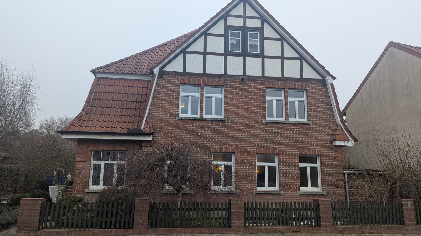 Außenansicht eines roten Ziegelhauses mit fachwerk-giebel, weißen Fenstern und Zaun