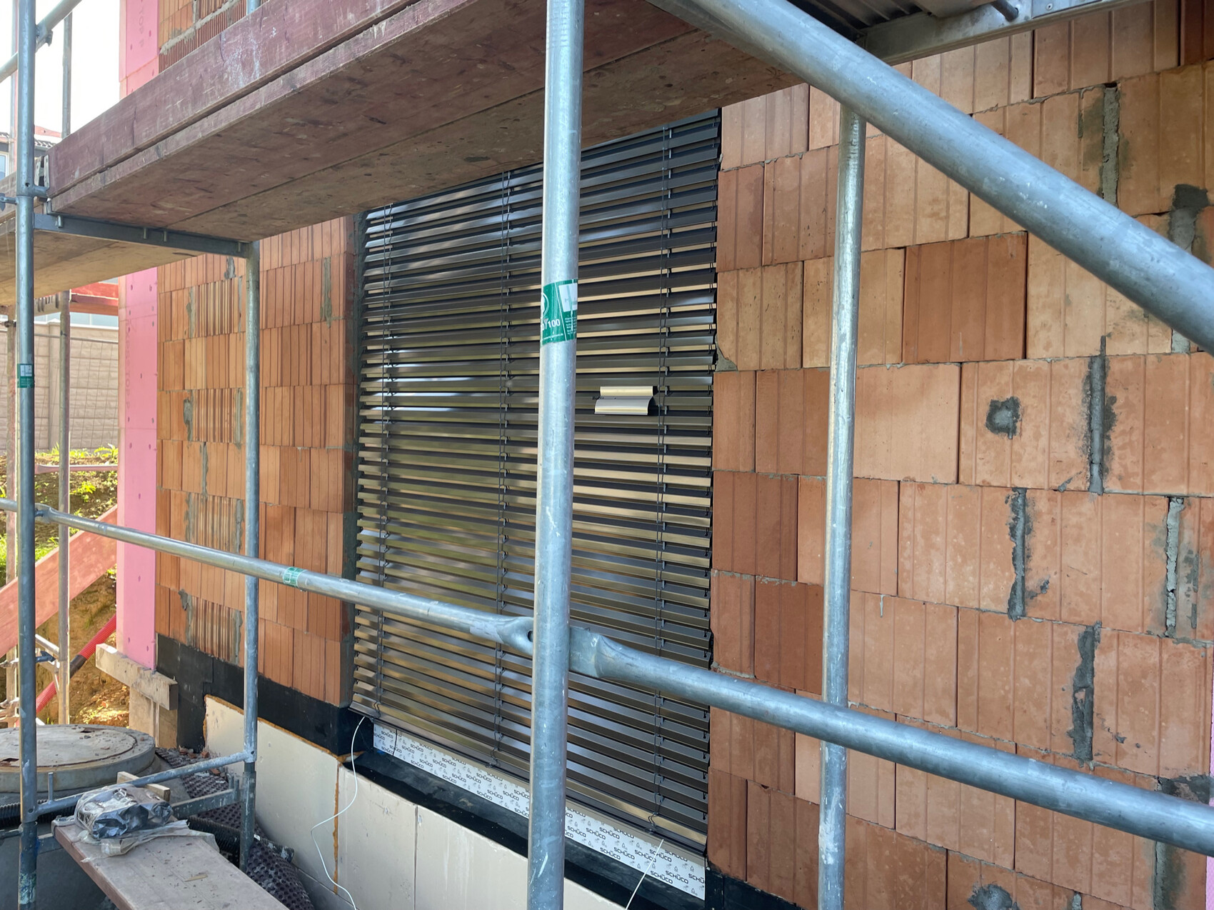 Baustelle: Gerüst vor einer Ziegelwand; Fenster mit horizontalen Metall-Lamellen.