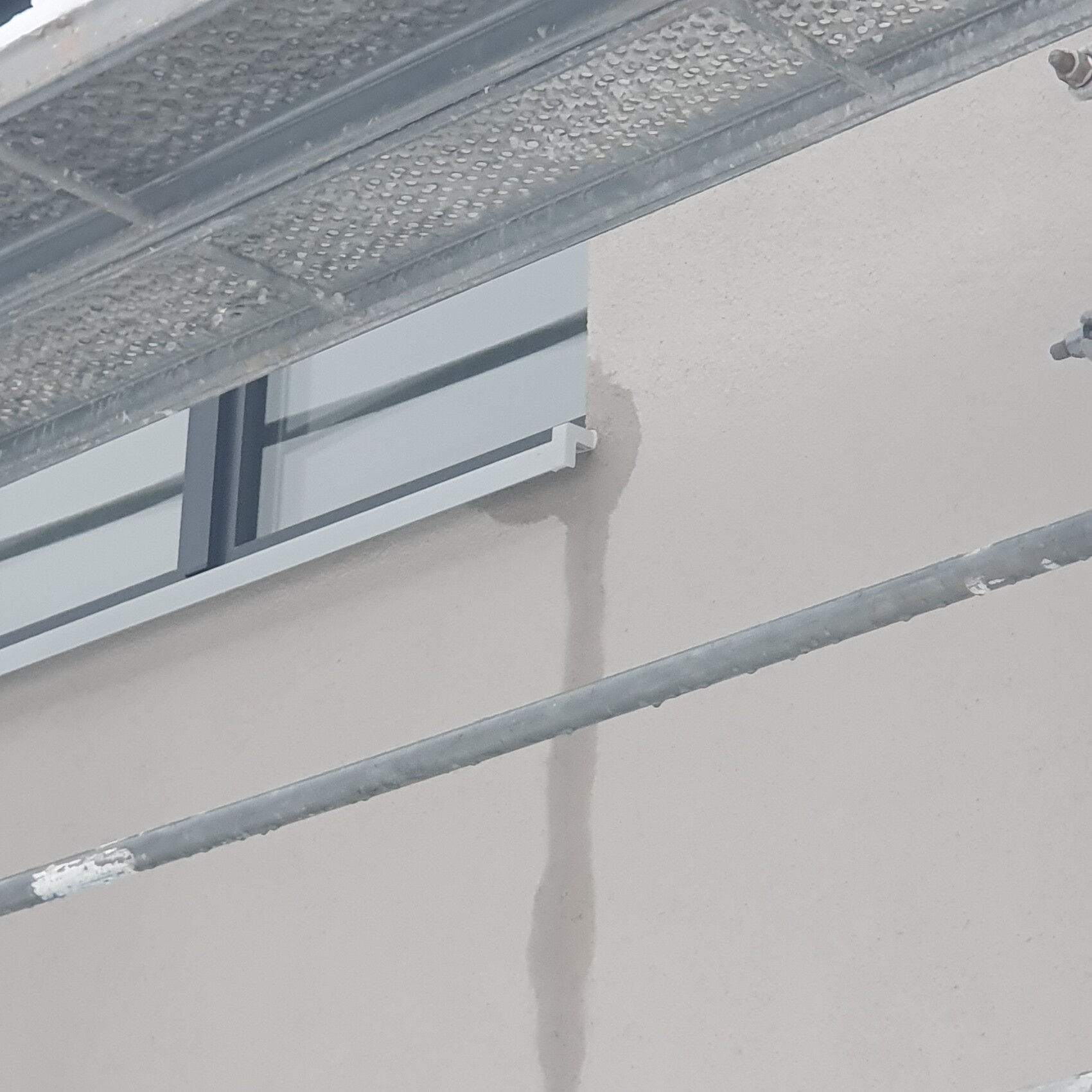 Außenwand mit kleinem Fenster, Feuchteverfärbung an der Wand und Gerüststangen davor.