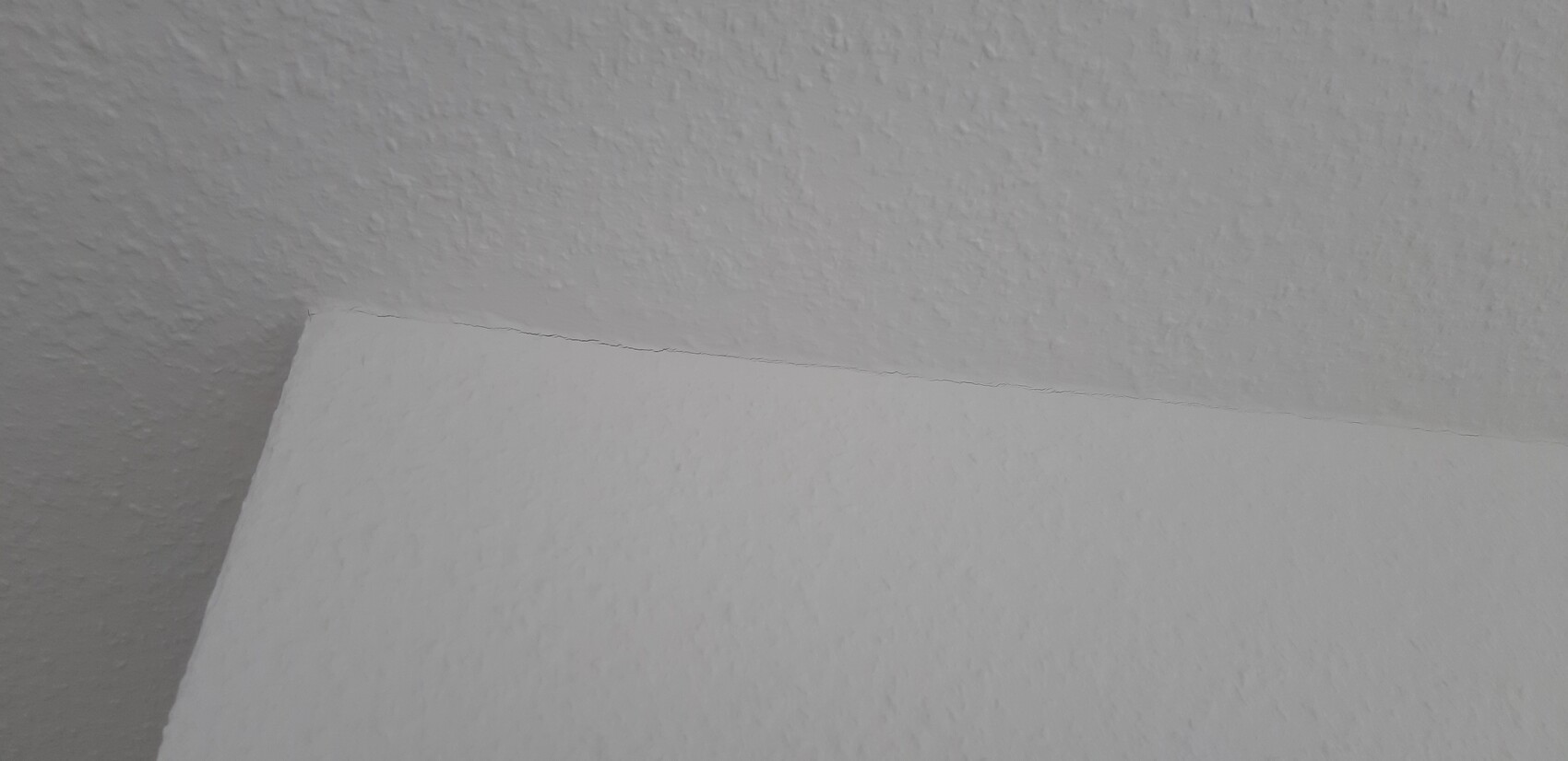 Nahaufnahme der rauen Textur einer Decken-Wand-Verbindung mit feiner Risslinie.