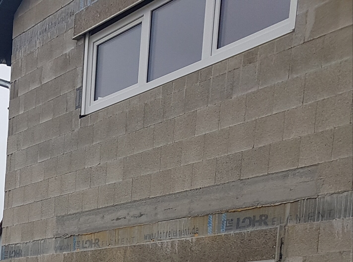 Außenwand aus Betonblöcken mit weißem Fensterrahmen; unten Bauband sichtbar.