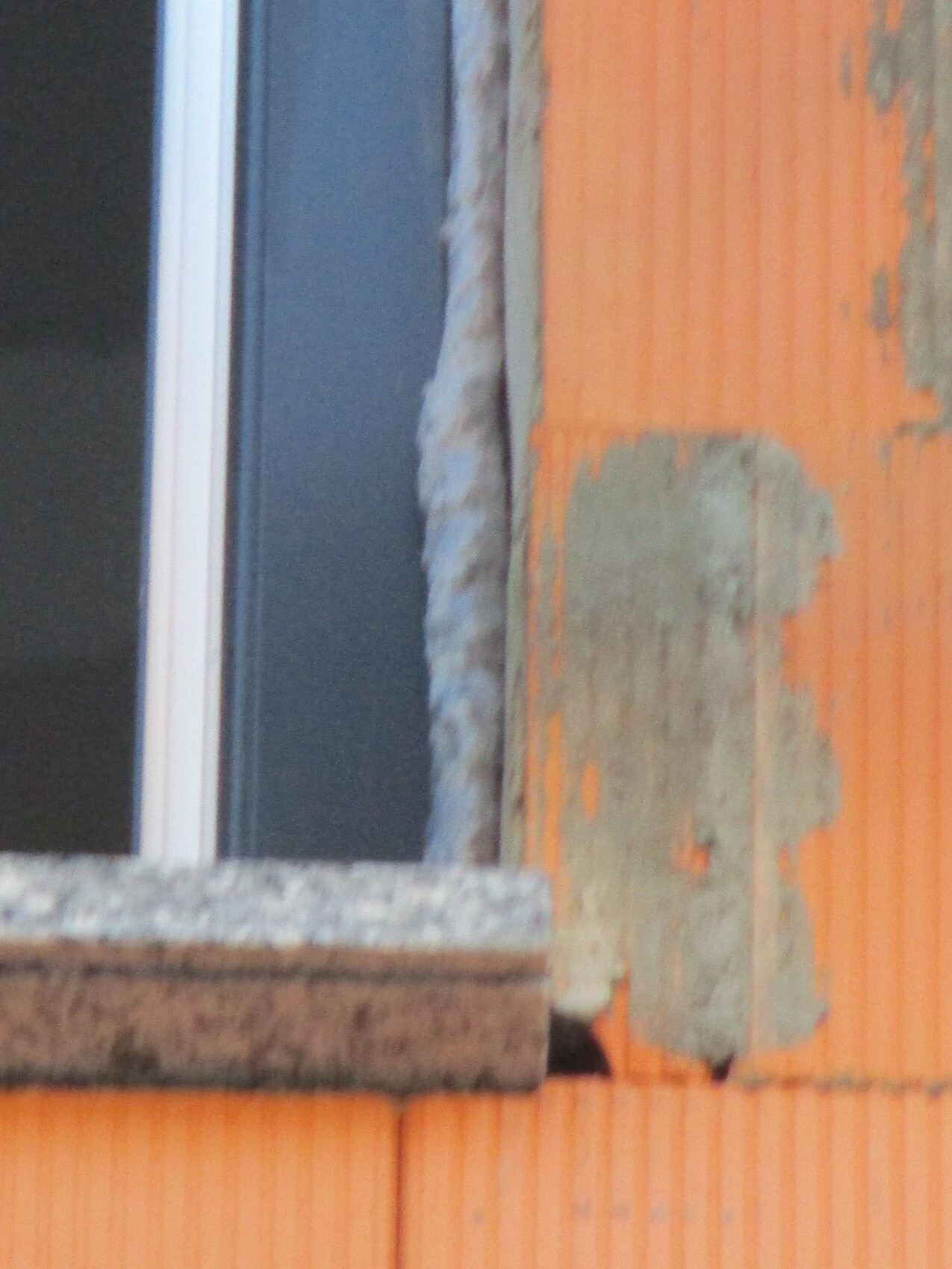 Nahaufnahme eines Fensterrahmens an einer orange verputzten Wand mit abblätterndem Putz.