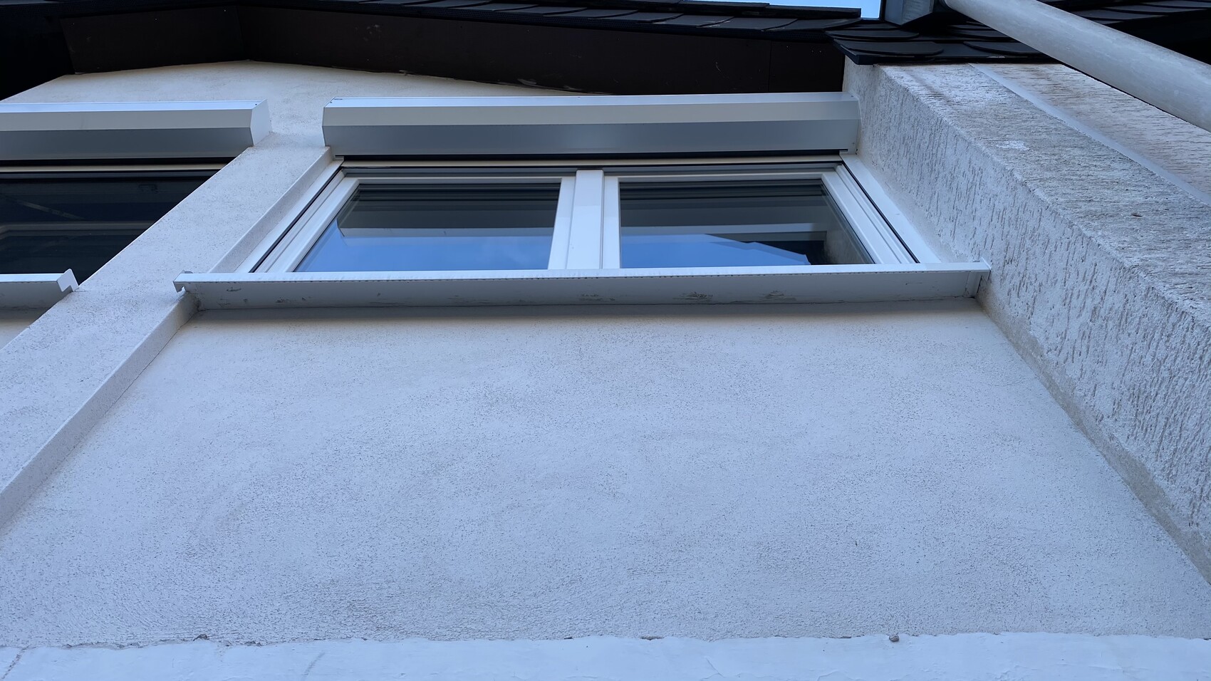 Außenfenster an weißer Putzfassade, Doppelfenster mit Fensterbank, blaue Himmelreflexion.