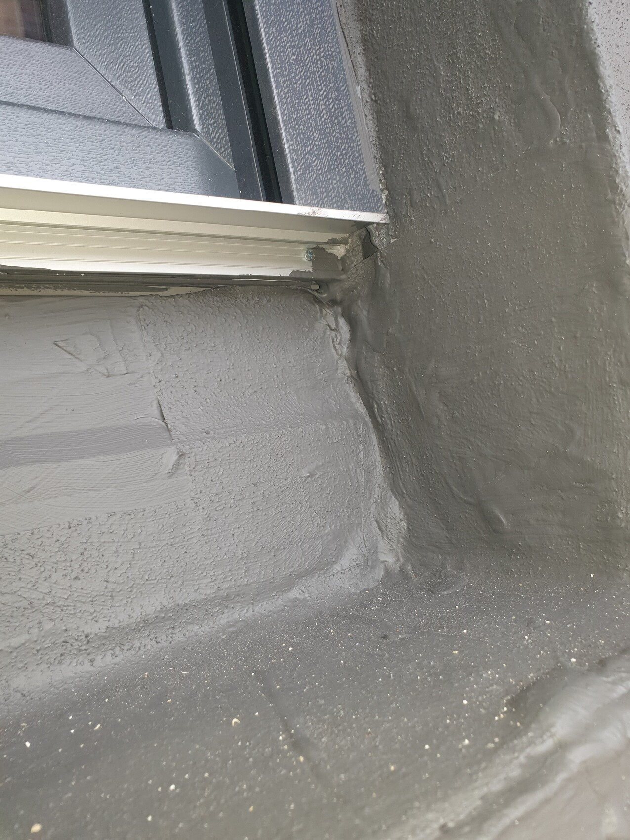 Nahaufnahme: Dachfenster mit grauer Dichtmasse am Fensteranschluss auf dem Dach.