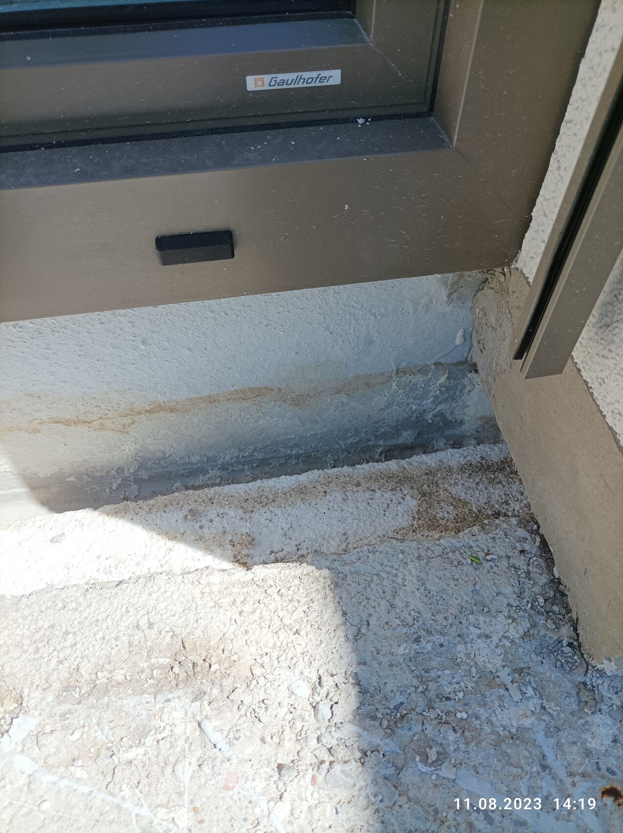 Außenfensterrahmen in dunkler Farbe, sichtbares Fundament und rauer Bodenbelag