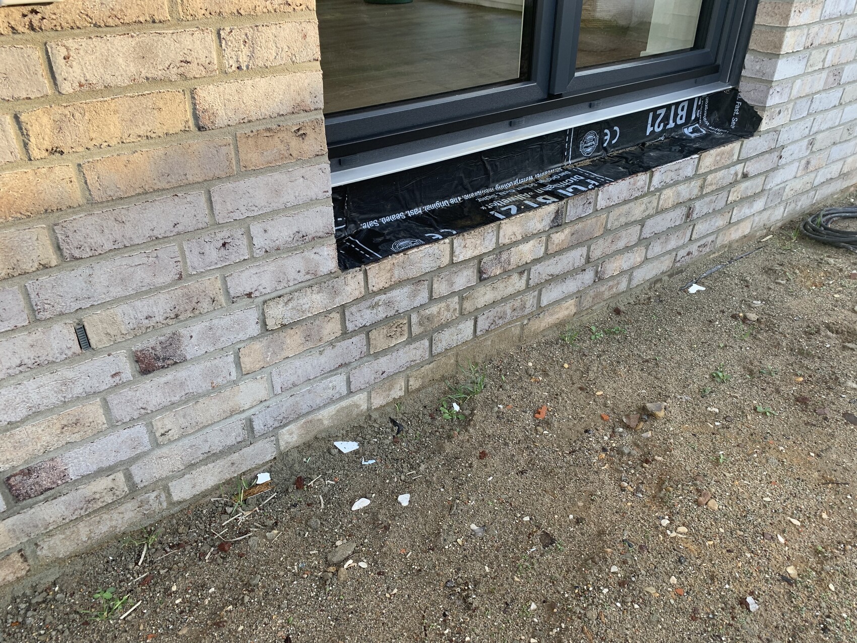 Außenwand aus hellen Ziegeln; Fenster mit schwarzem Dichtband darunter.