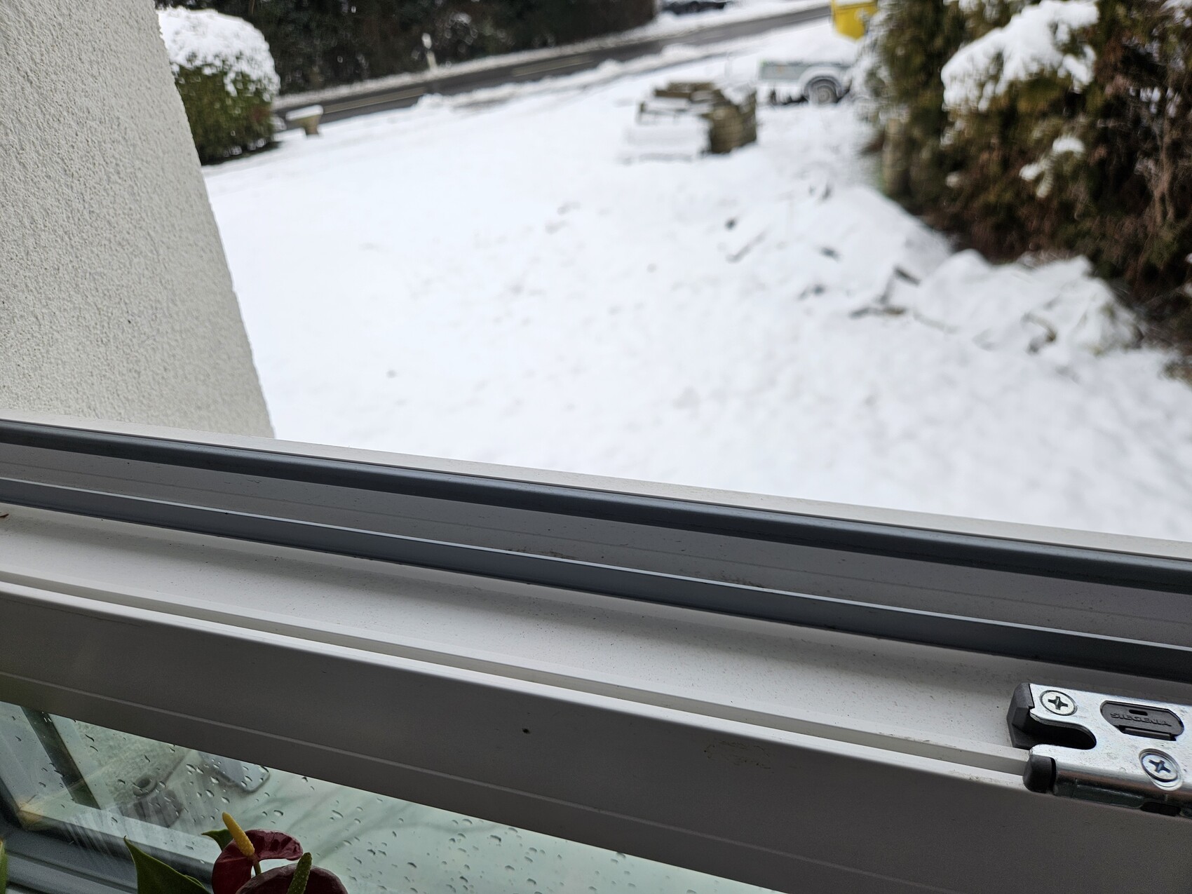 Blick aus dem Fenster auf eine verschneite Außenfläche mit Auto im Hintergrund.