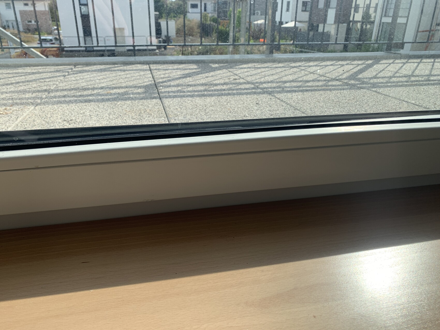 Innenfensterbank aus Holz, Blick auf Balkongeländer, Straße und Gebäude außerhalb.