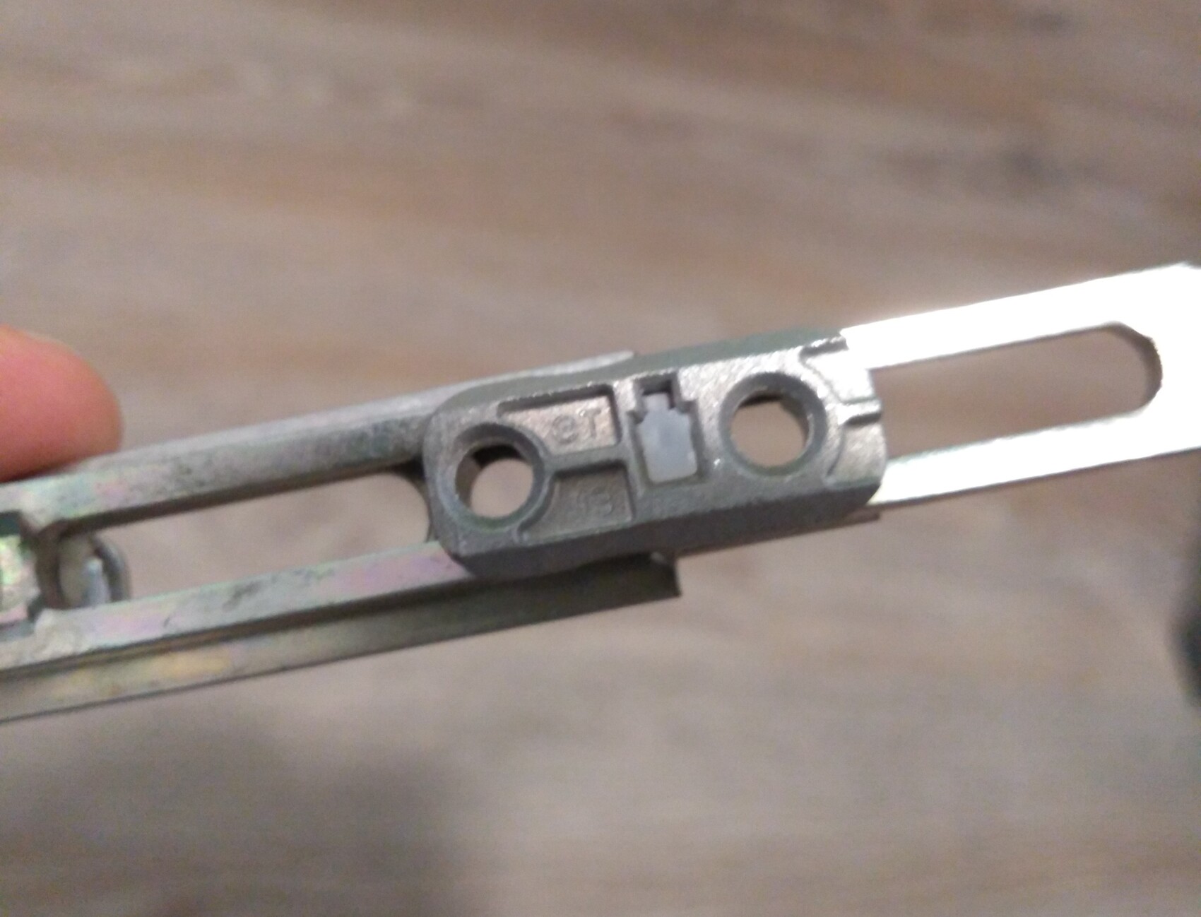 Nahaufnahme eines metallischen Bauteils mit zwei runden Löchern und grauer Kunststoffführung.
