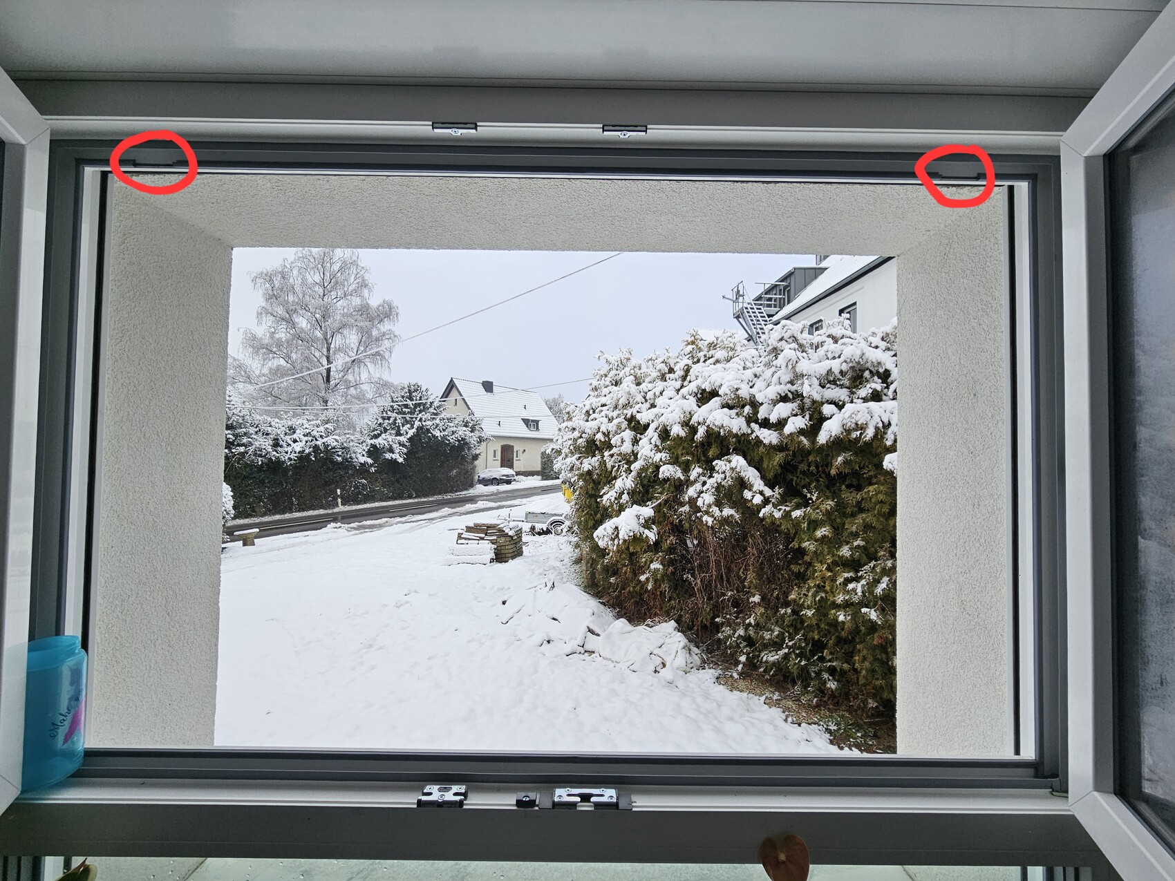 Fensterblick auf verschneite Straßenszene mit Hecken und Häusern im Winter