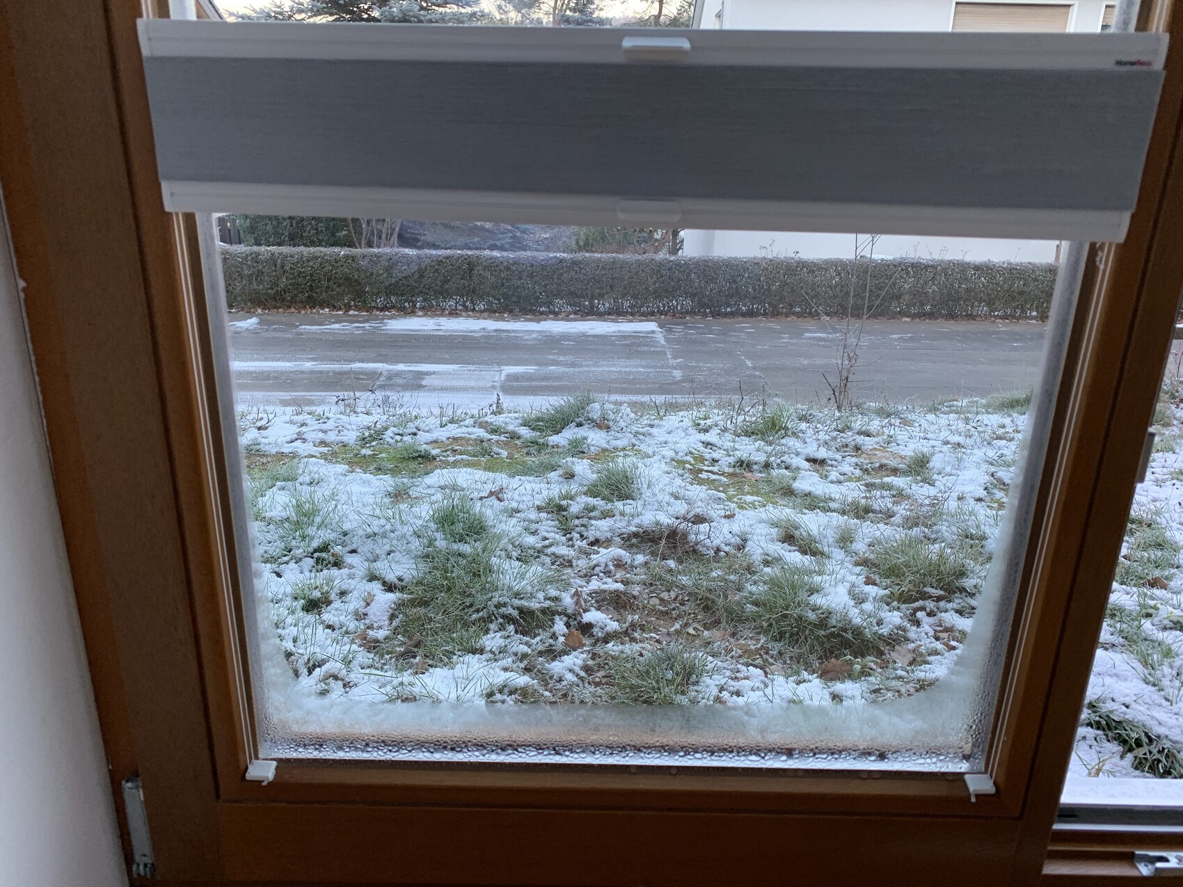 Blick von innen durch ein Fenster mit heller Rollladen-Jalousie auf verschneite Außenfläche