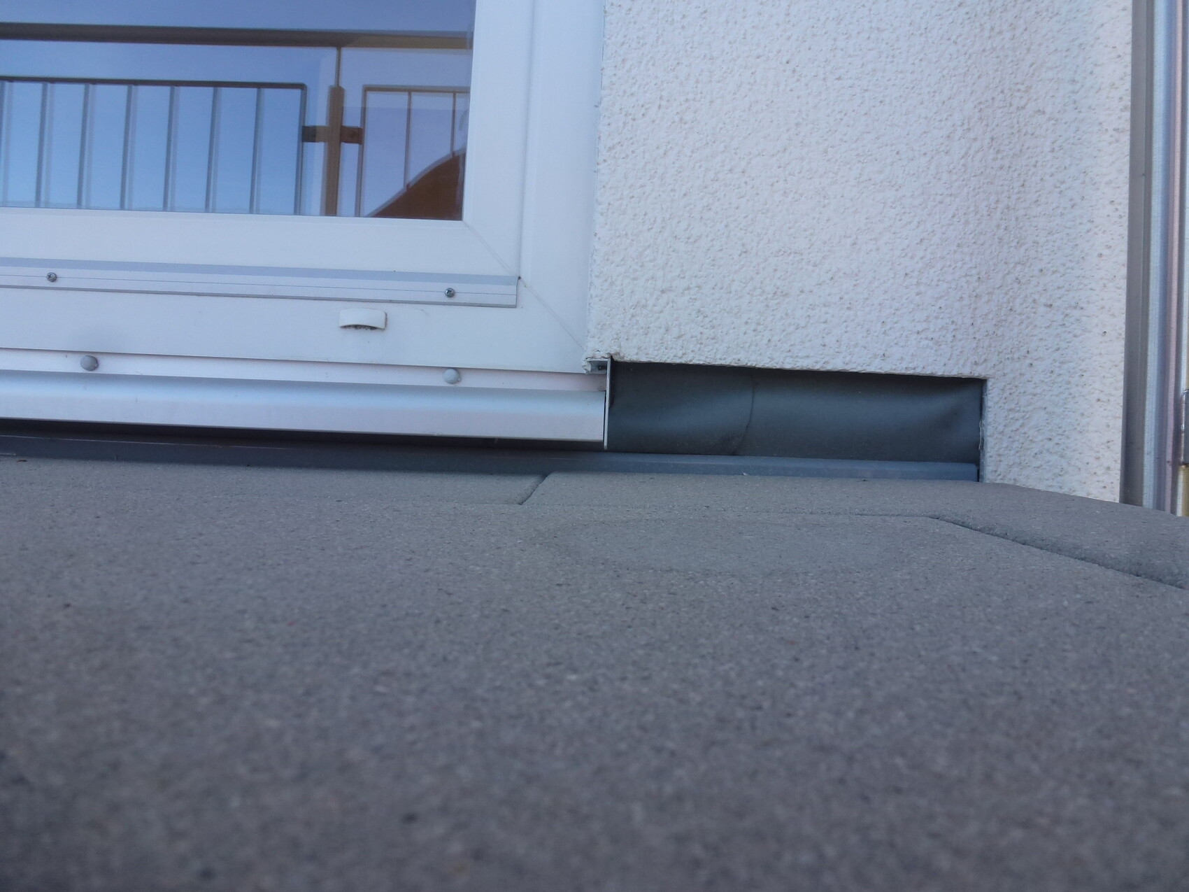 Weißer Fensterrahmen vor strukturierter Putzwand; Flachdachkante im Vordergrund.