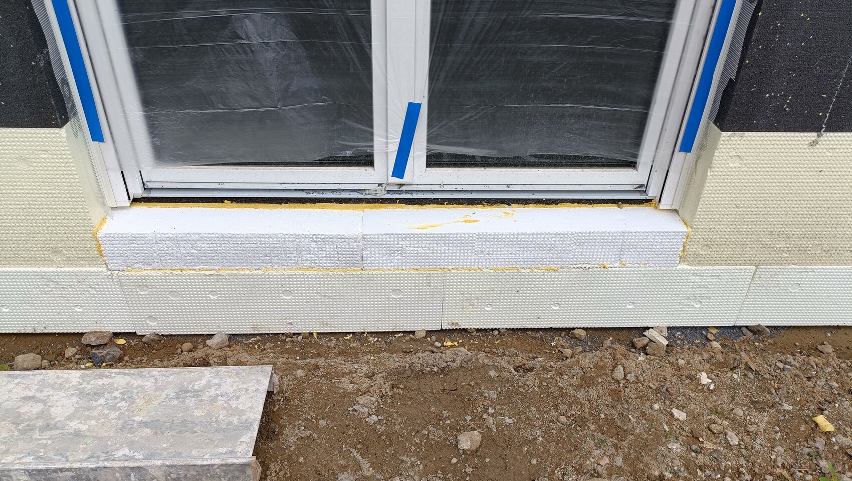 Fensterrahmen in Bauphase, umgeben von weißen Styroporplatten; blaues Klebeband am Rahmen.