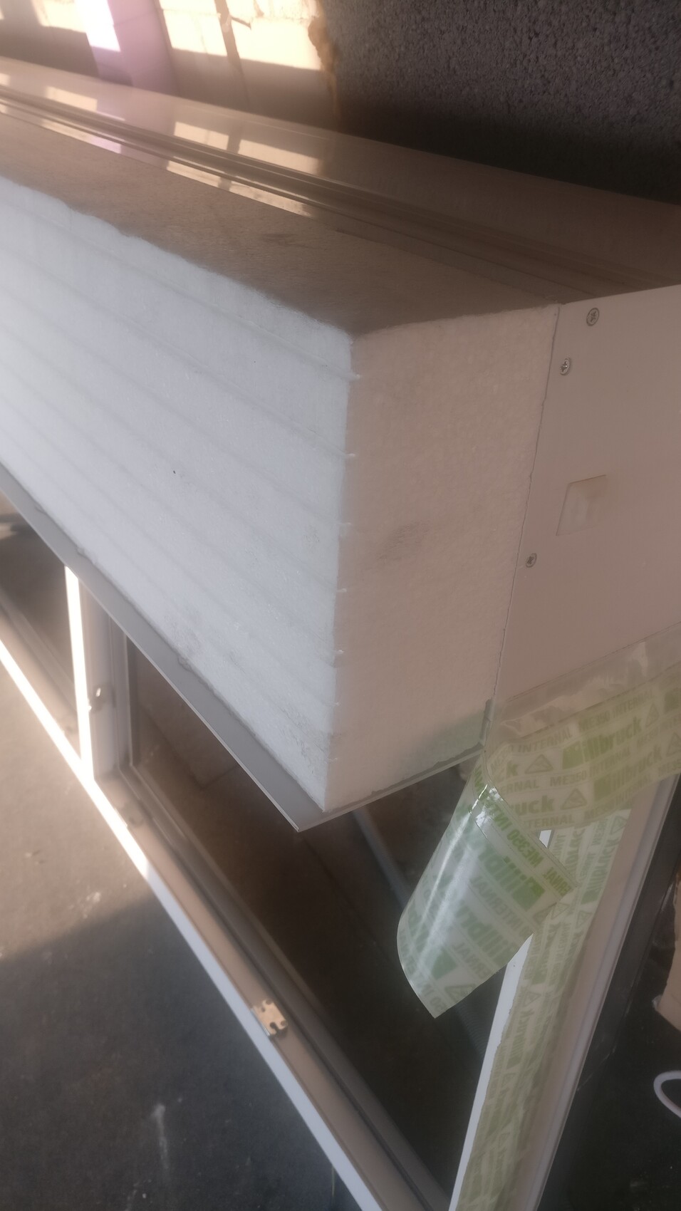 Nahaufnahme eines Fensterrahmens mit weißem Dämmblock aus Styropor und Klebeband