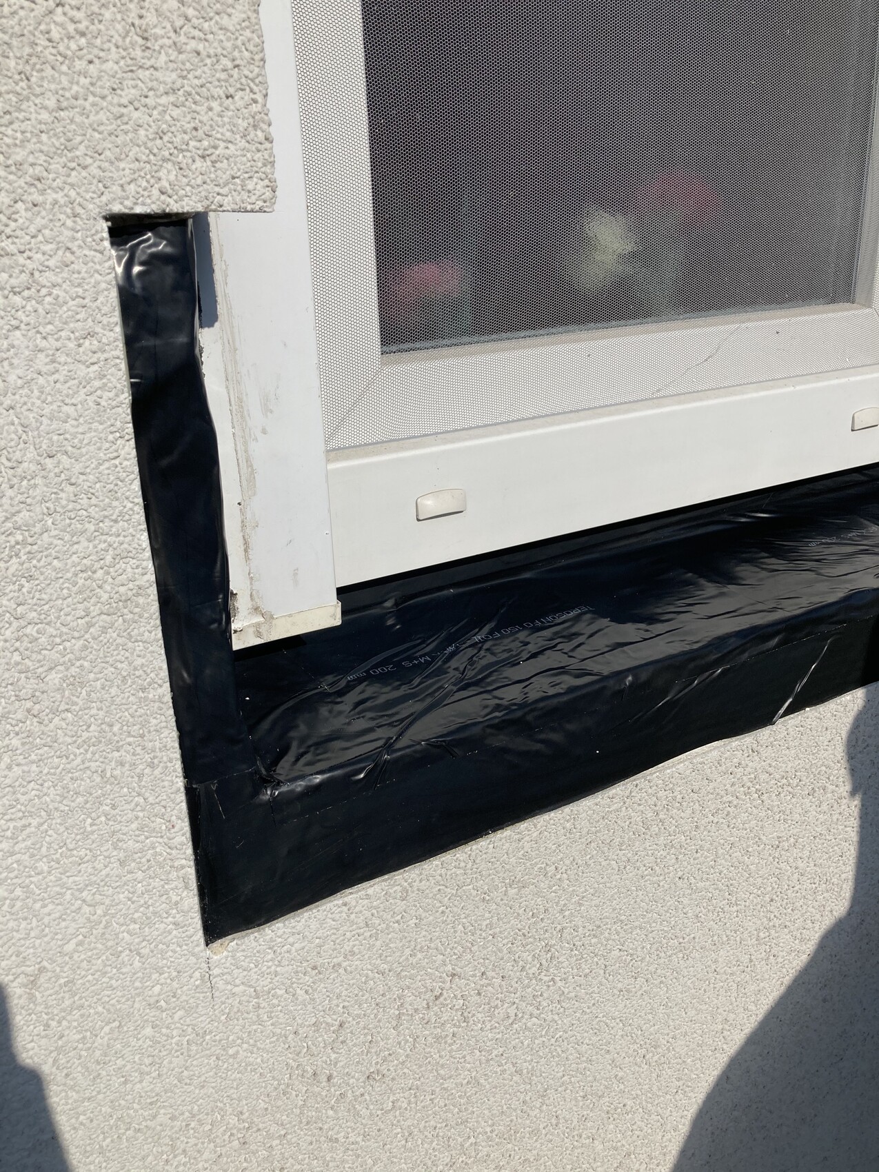 Außenfenster mit weißem Rahmen, Fliegengitter, darunter schwarzes Abdichtband am Fensterbank