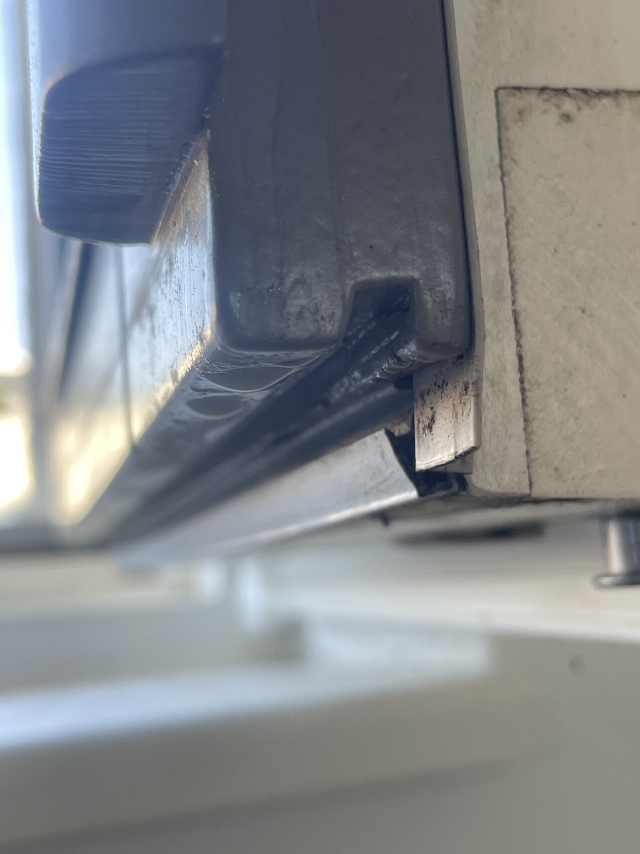 Nahaufnahme einer beschädigten Metallkante mit abgeplatzter Lackschicht und sichtbarer Dichtung.