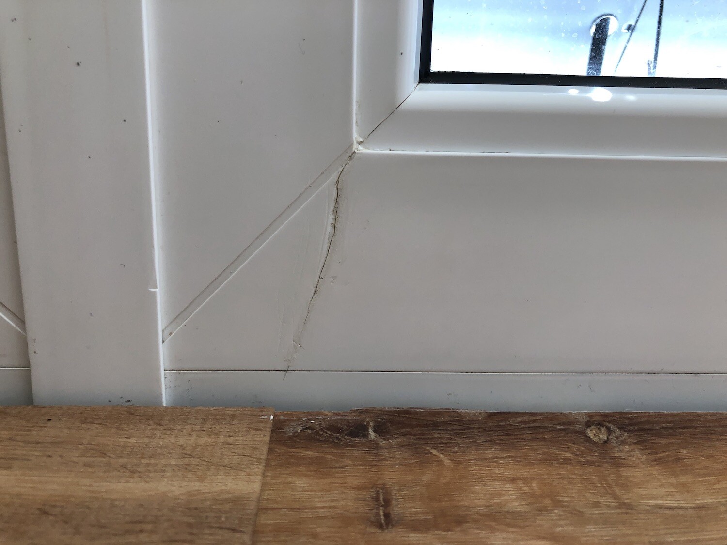 Ecke eines weißen Fensterrahmens mit Spalt an der Leiste, Holzfußboden unten.