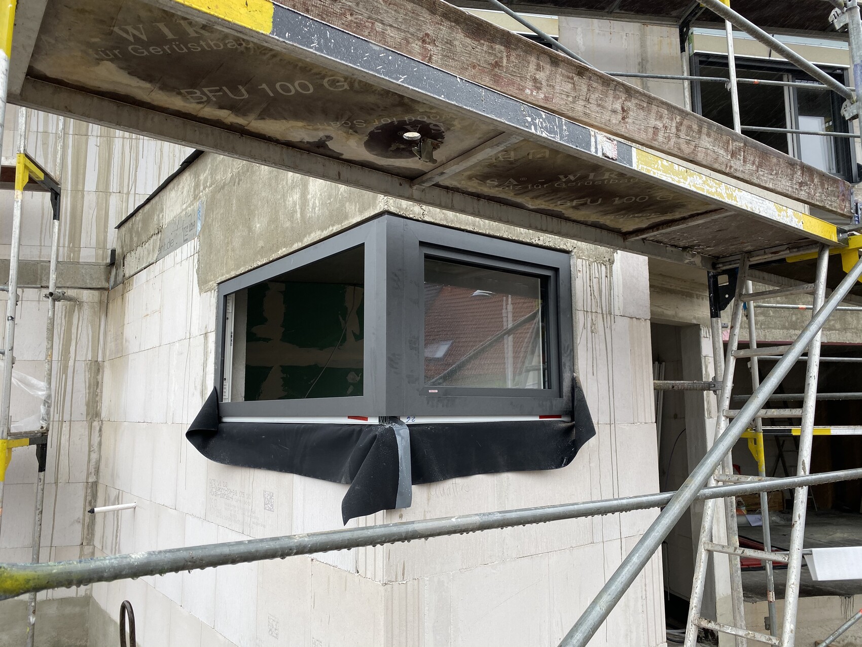 Neues Fenster in verputzter Fassade, umlaufendes Gerüst und schwarzer Abdeckstoff darunter.