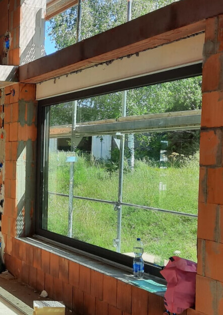 Baustellenfenster in Ziegelwand, außen Gerüst, Wasserflasche auf Fensterbank.