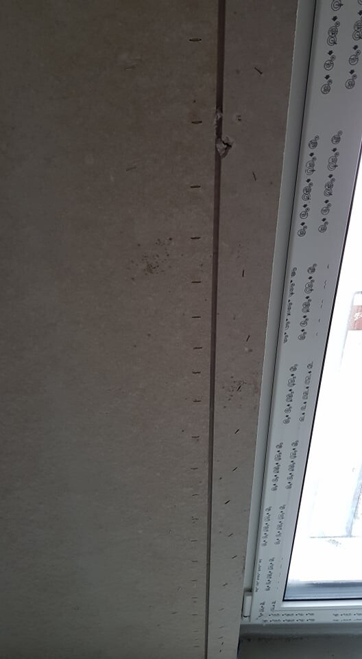Unfertiger Fensterrahmen im Rohbau, sichtbare Befestigungslöcher in der Wand