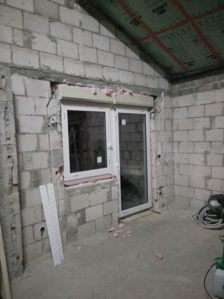 Renovierungsraum mit unfertigen Blockwänden, Fenster- und Türrahmen, Dämmmaterial und Kabelrollen.
