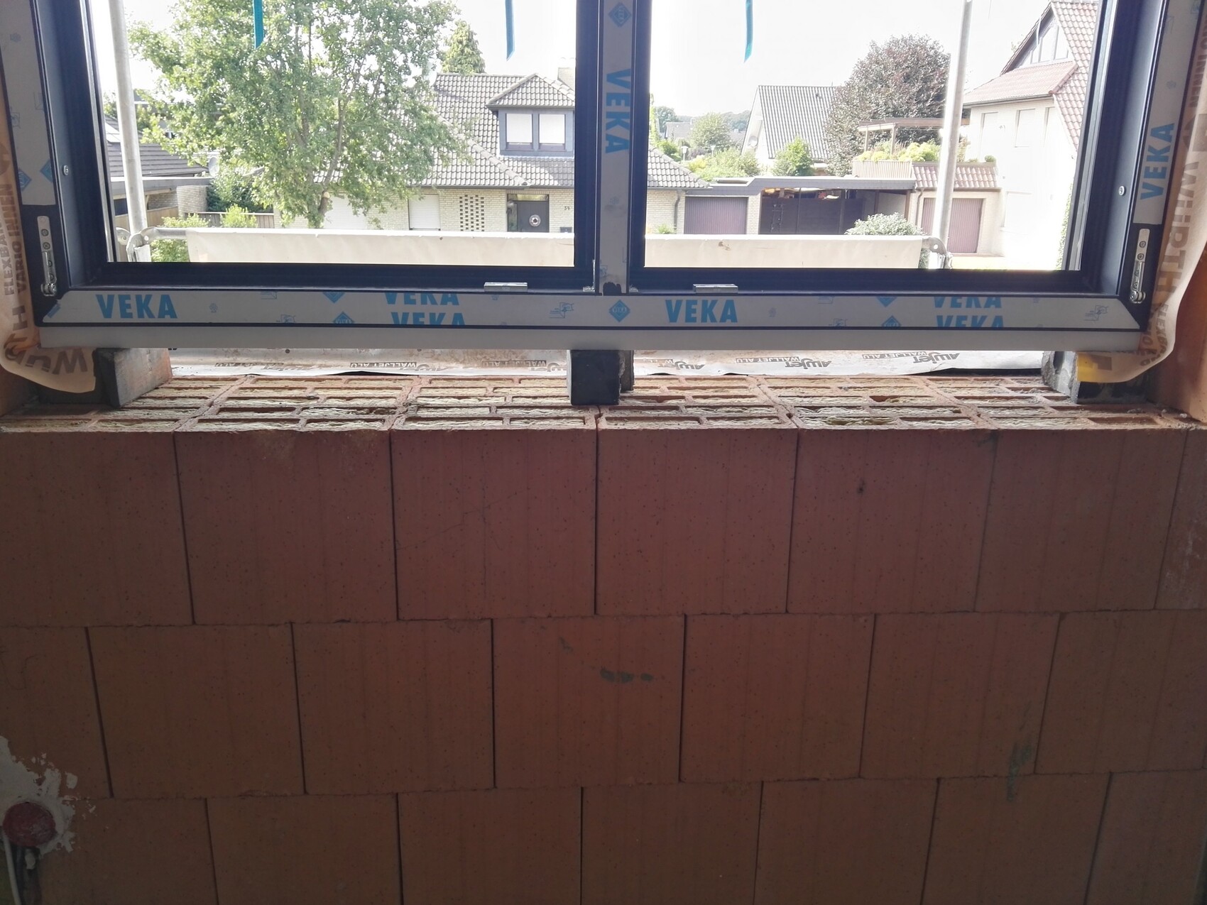 Offenes Fenster in roter Ziegelwand; Innenraum im Bau, Blick auf Nachbarhäuser.