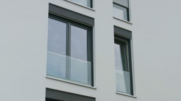 Weiße mehrstöckige Gebäudefassade mit zwei Fenstern und Glasbalkon