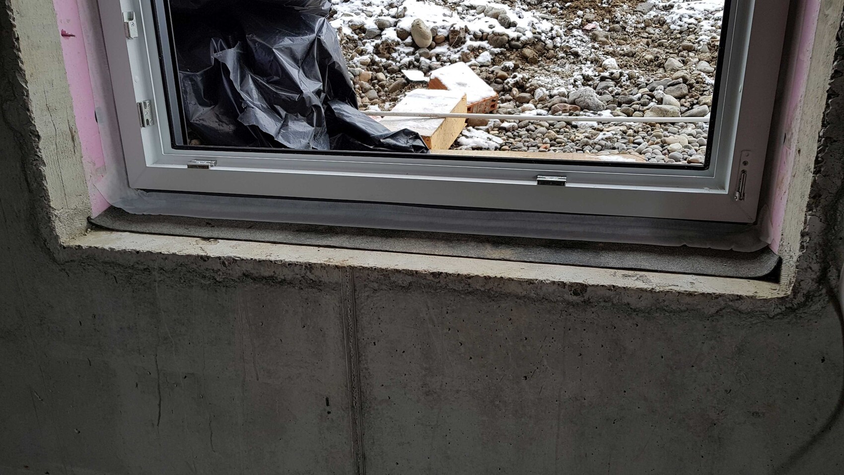 Fenster im Rohbau in Betonwand, Außenseite mit Bauschutt und Kies.