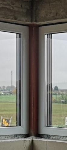 Zwei Fenster im Rohbau-Korner mit roter Standsäule, Blick auf Felder